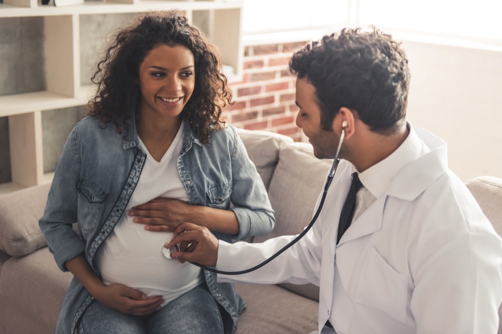 American doctor in white coat is consulting beautiful pregnant woman